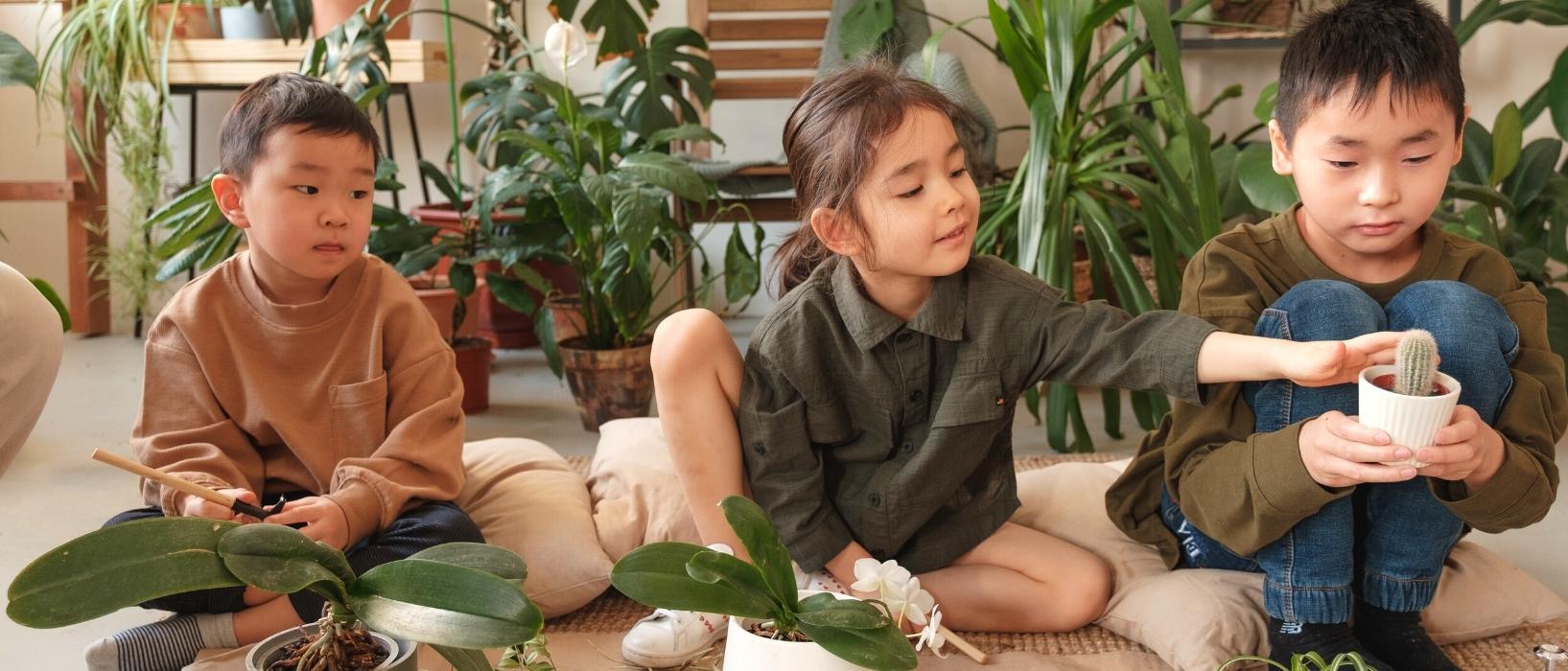 three kids sitting in a row holding plants, earth month education