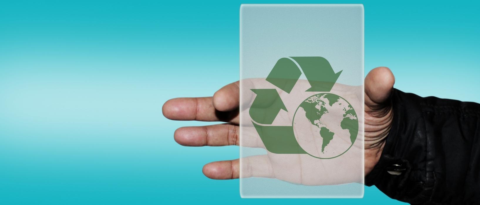 hand holding transparent piece of glass with sustainability symbol on it (green triangle with earth in centre)