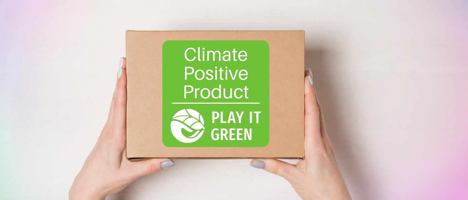 woman holding a cardboard box with Play it Green Climate Positive Product badge on it