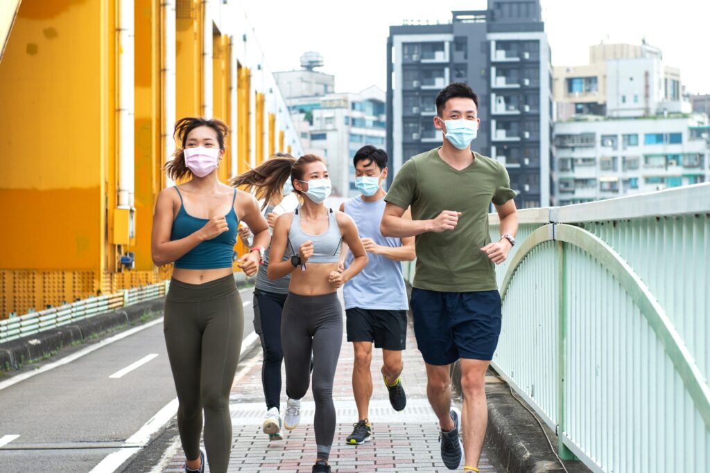 group of people jogging across pedestrian bridge in a city, all are wearing face masks