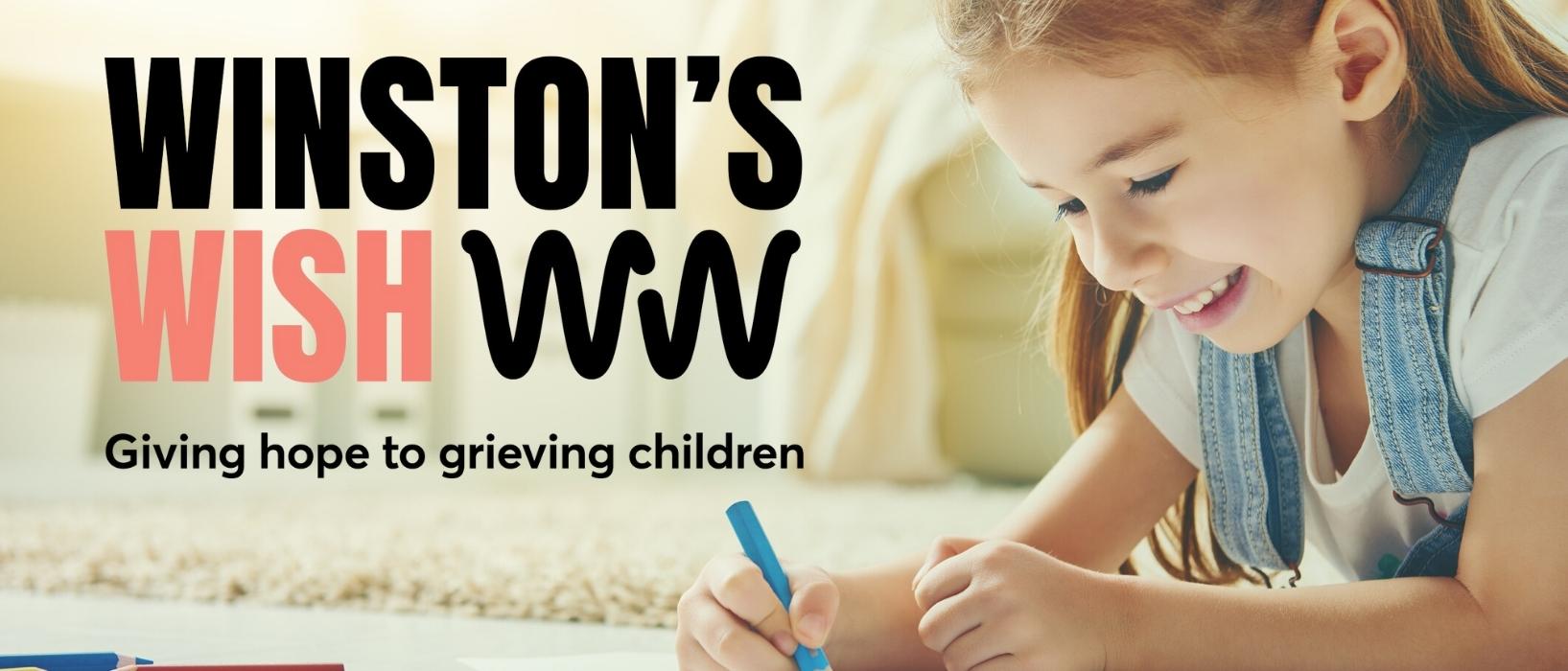young girl lying on floor drawing with coloured pencil and smiling, Winston's Wish logo beside her
